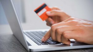 Homme avec sa carte bancaire à la main entrain de passer une commande en ligne sur son ordinateur
